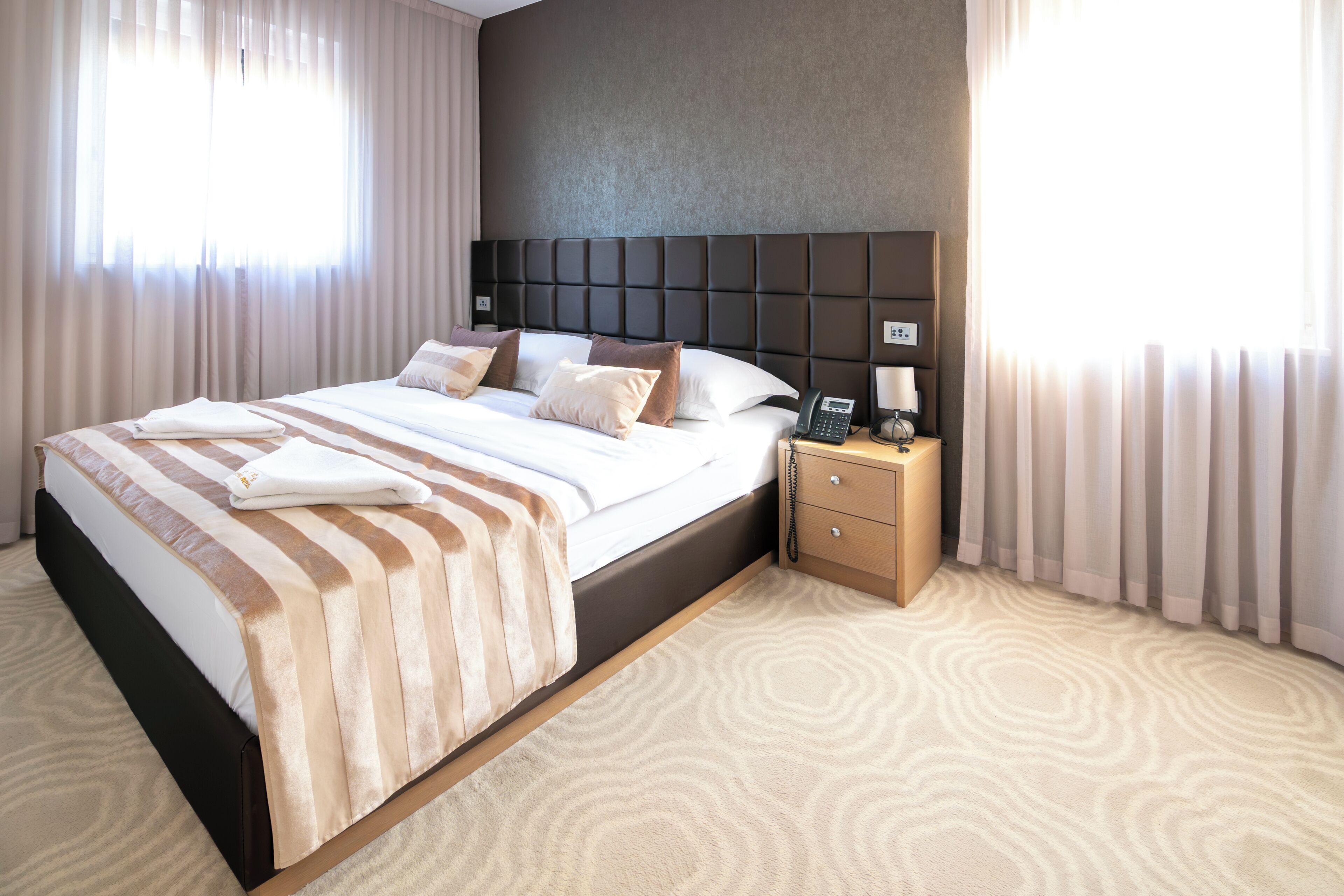 A hotel room with a large bed, a bedside table with a phone, and a headboard.
