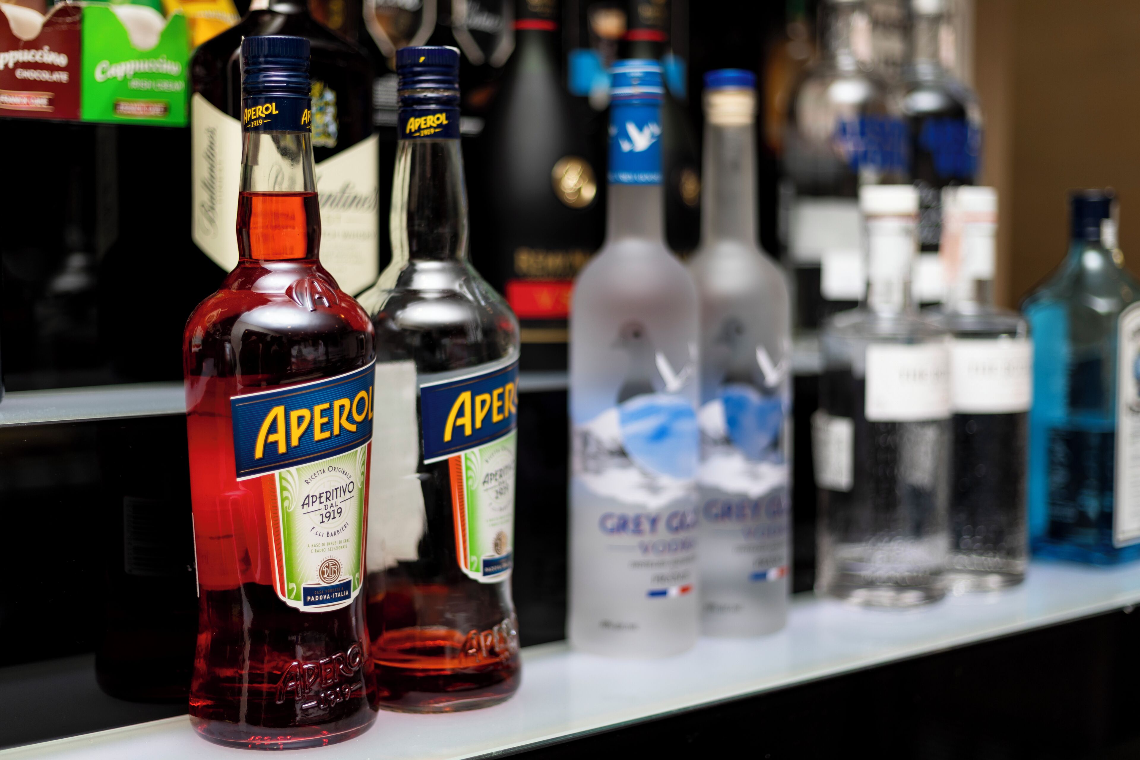 A shelf with various bottles, including Aperol and Grey Goose vodka.