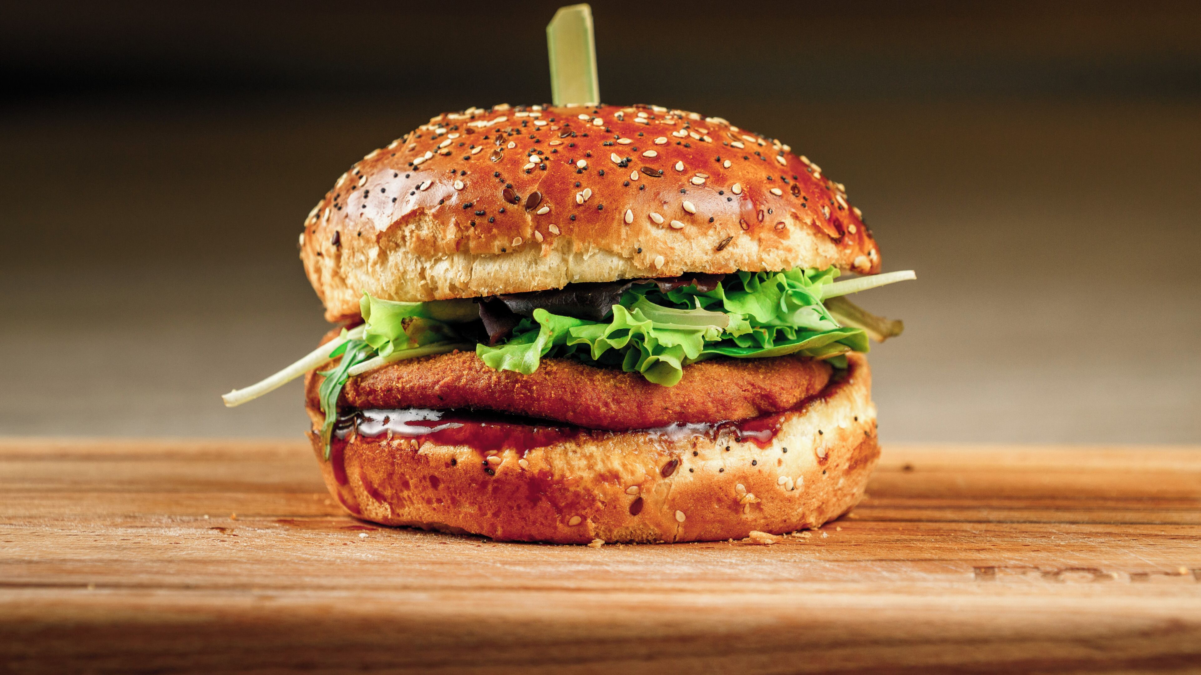 Un panino con pane ai semi di sesamo, lattuga e una polpetta fritta, su un piano di legno.