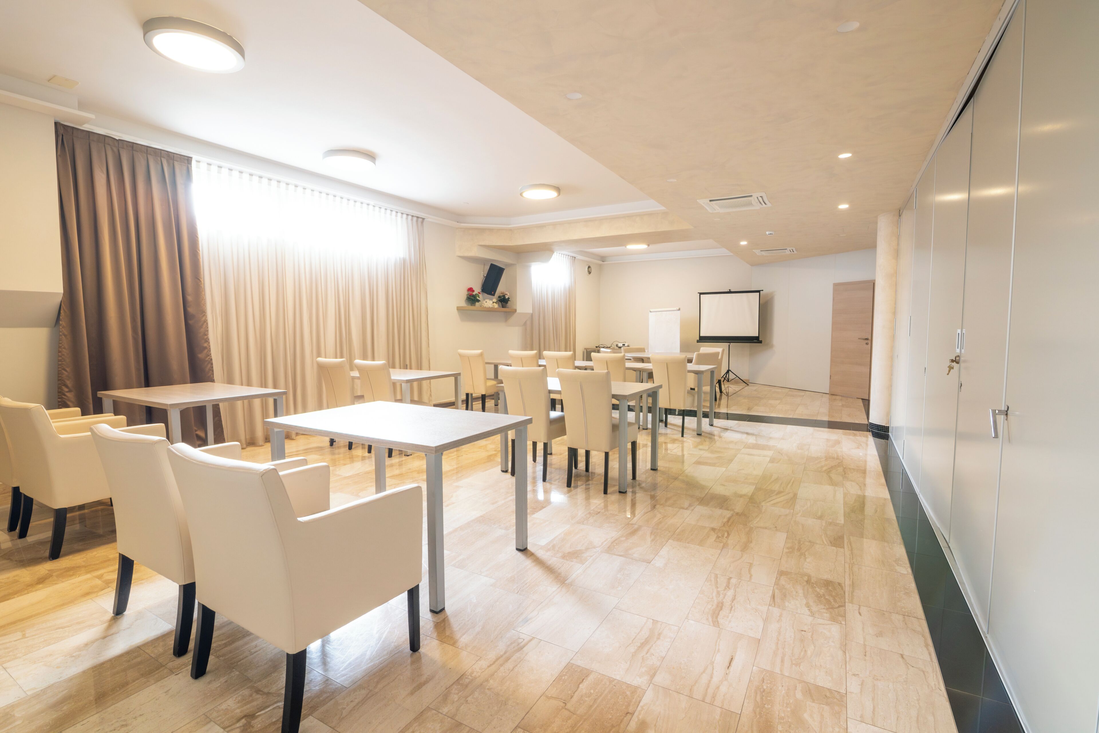 A conference room with tables and chairs, a projector screen, and a large whiteboard.
