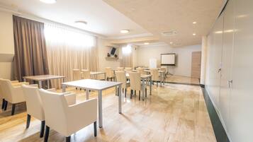 A conference room with tables and chairs, a projector screen, and a large whiteboard.
