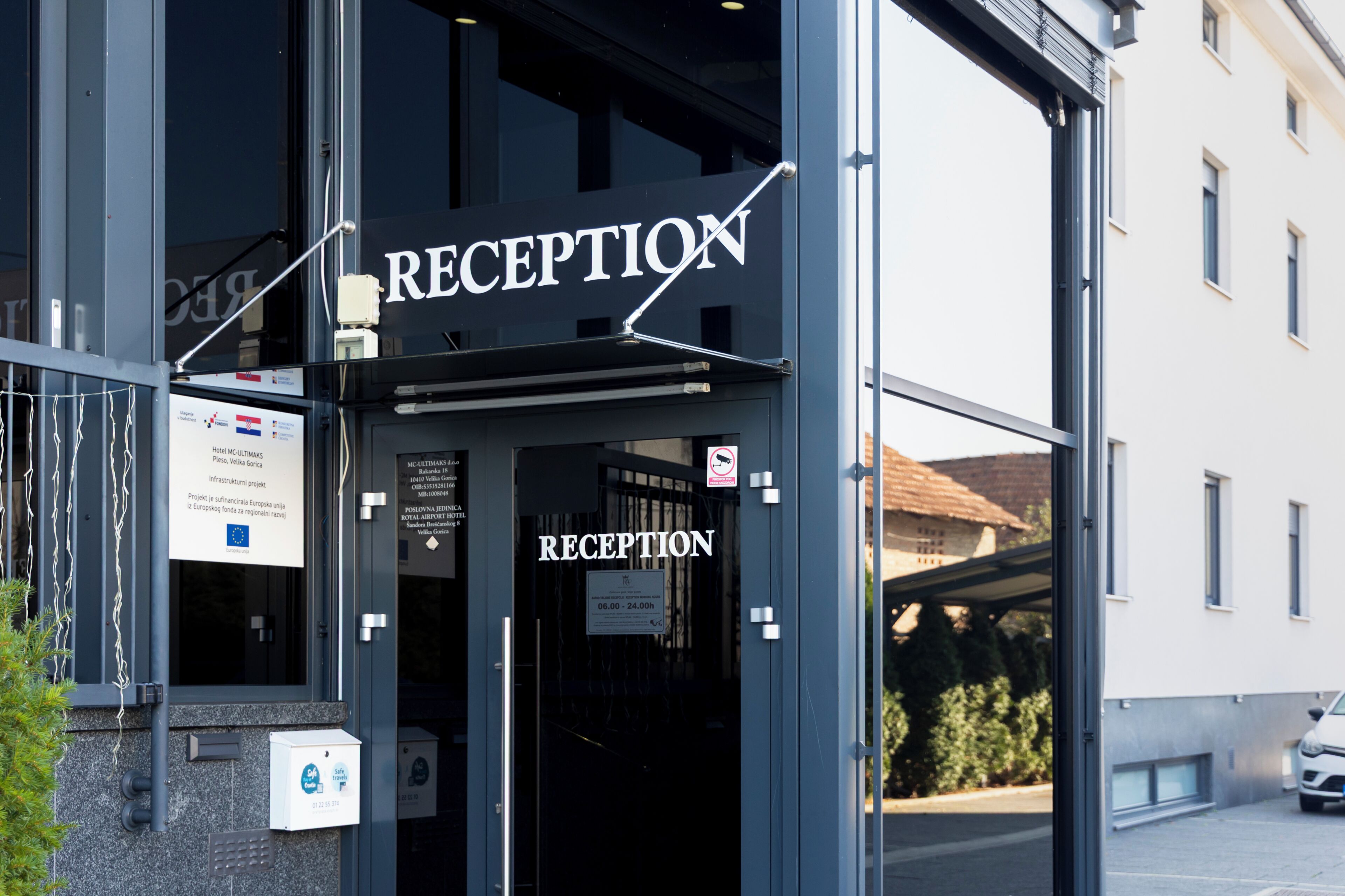 Un'area reception con un cartello, una porta in vetro e un parcheggio visibili.
