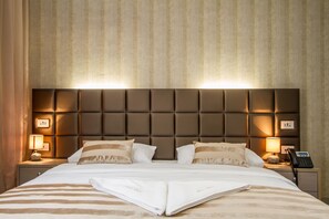 A neatly made bed with a striped bedspread, a headboard with illuminated panels, bedside lamps, and a telephone on the nightstand. - Royal Airport Hotel (Velika Gorica)