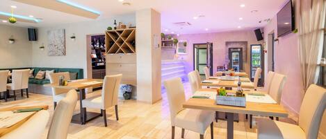 A modern restaurant with a long counter, multiple tables, and chairs.
