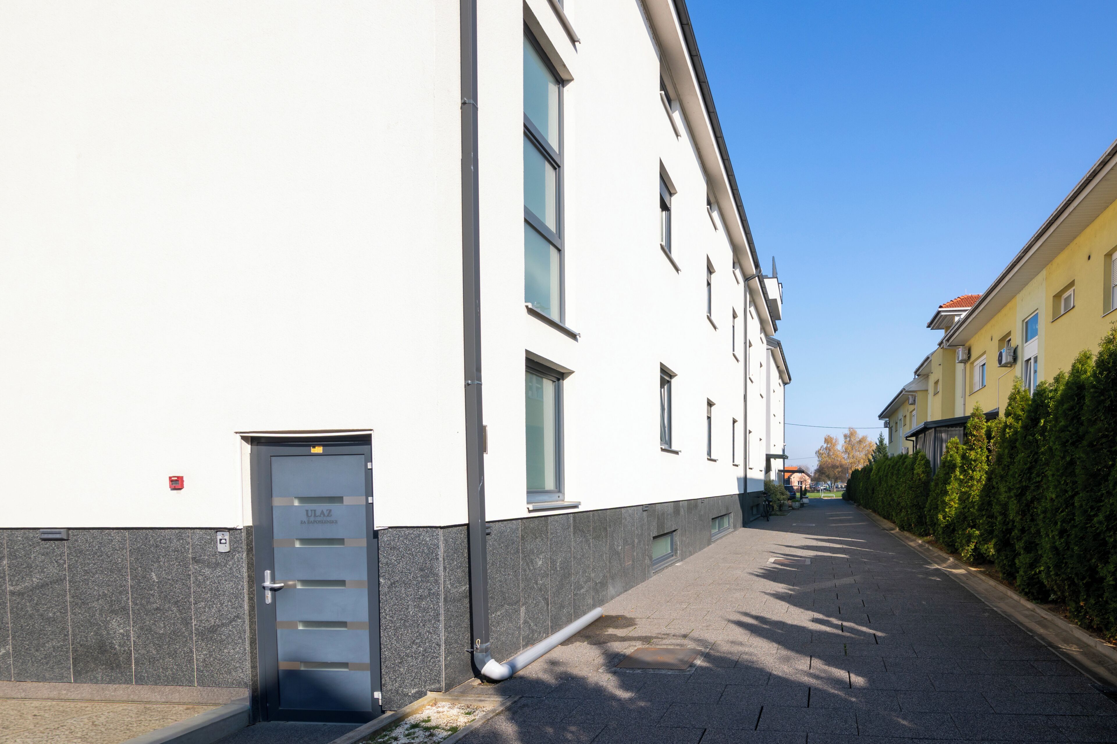 Une rue étroite, avec un bâtiment blanc sur la gauche et un bâtiment jaune sur la droite.