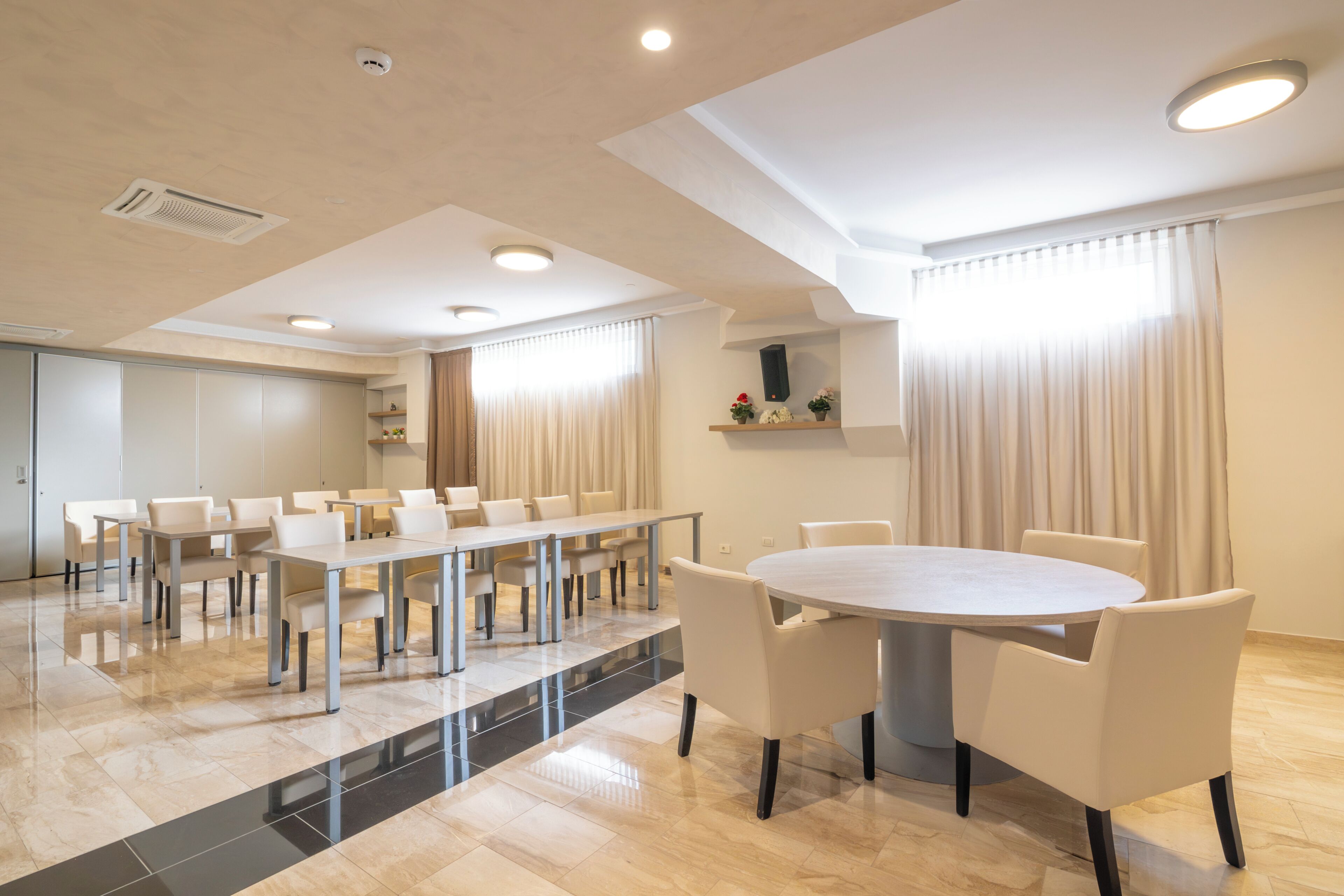Uma sala de conferências moderna com uma mesa comprida e cadeiras, uma mesa redonda menor e um sistema de som embutido.