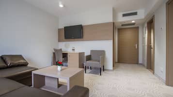 Een moderne hotelkamer met een bank, een klein tafeltje met een vaas, een stoel, een aan de muur bevestigde televisie en een deur.