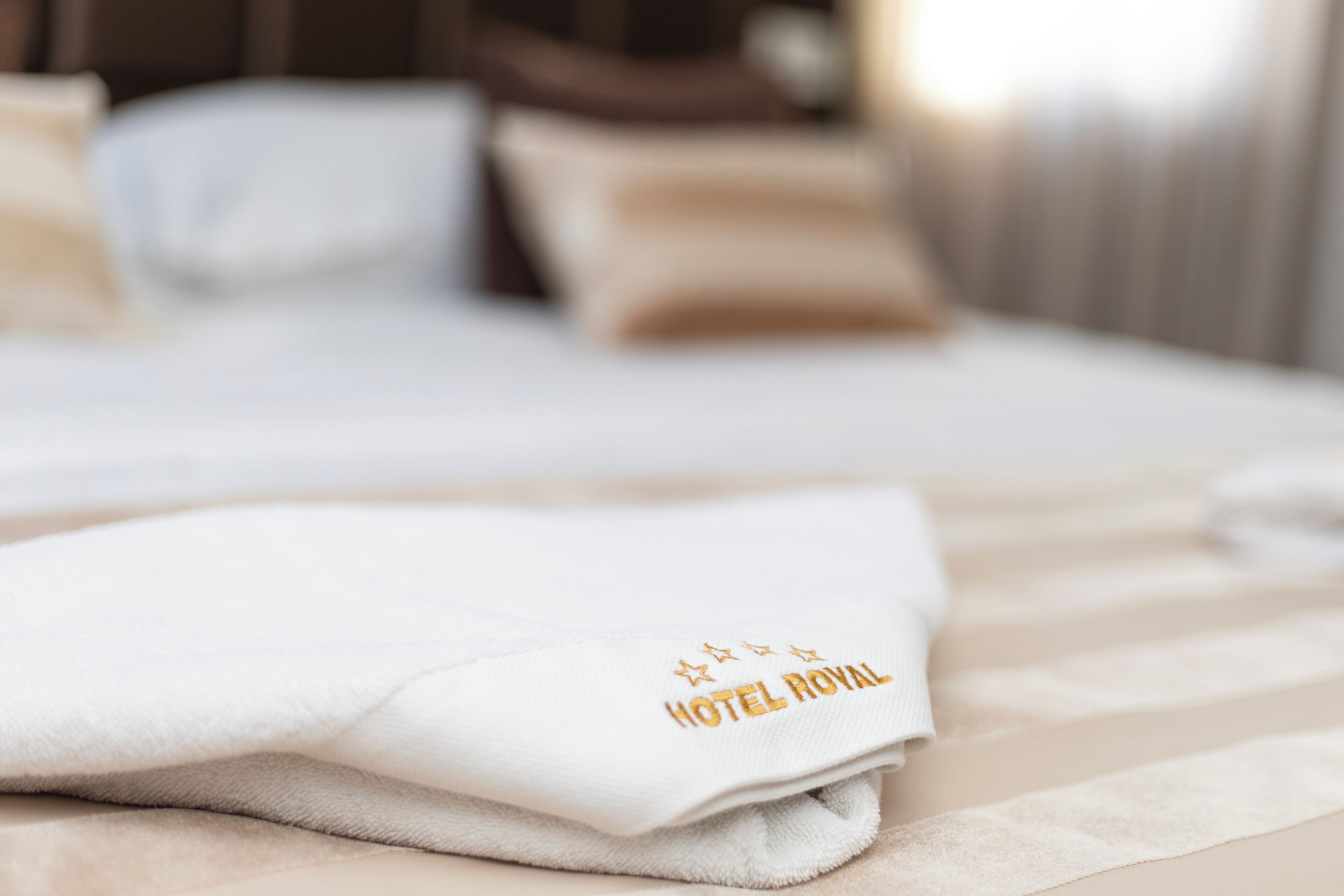 A neatly folded white towel with 'HOTEL ROYAL' embroidered on it, placed on a bed with a striped bedspread.