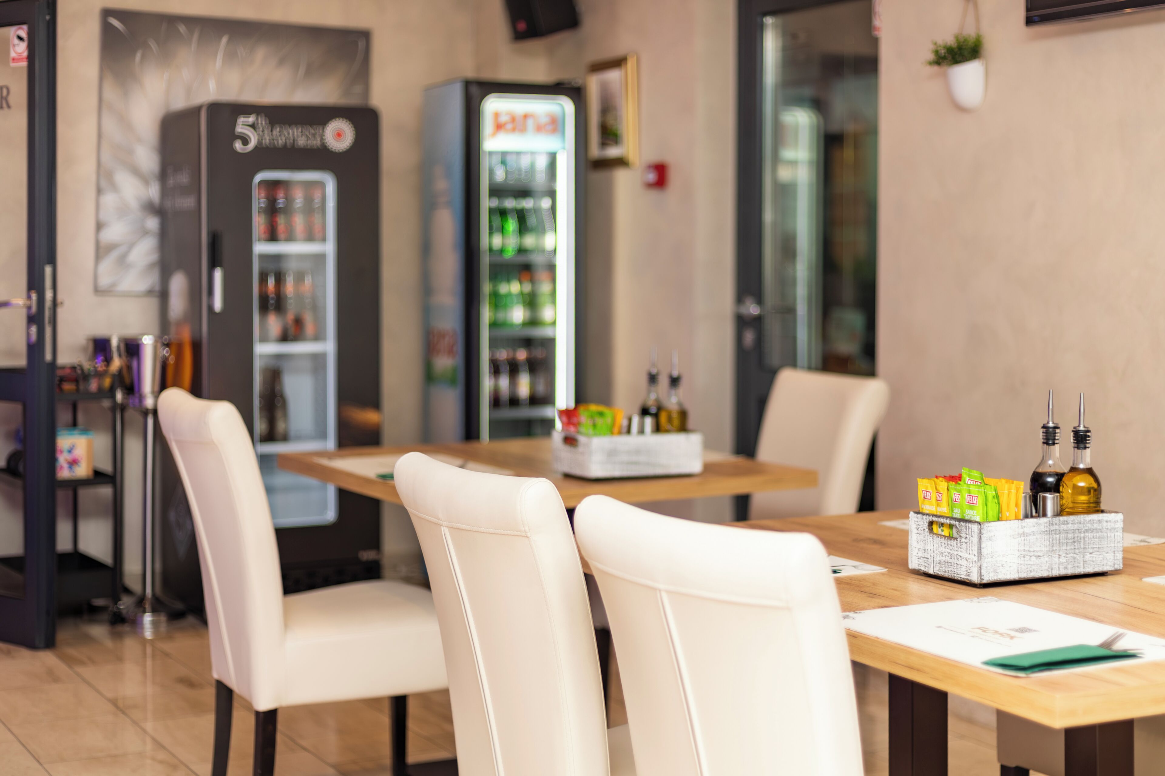 Un interior de restaurante con una mesa de madera, sillas blancas, una máquina expendedora y un refrigerador.