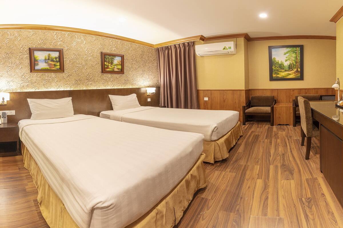 A hotel room with two beds, a desk, a chair, and a small table.