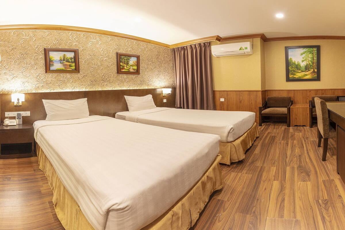 A hotel room with two beds, a desk, a chair, and a painting on the wall.
