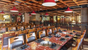 Een restaurant met meerdere tafels en stoelen, houten balken in het plafond en rode hanglampen.