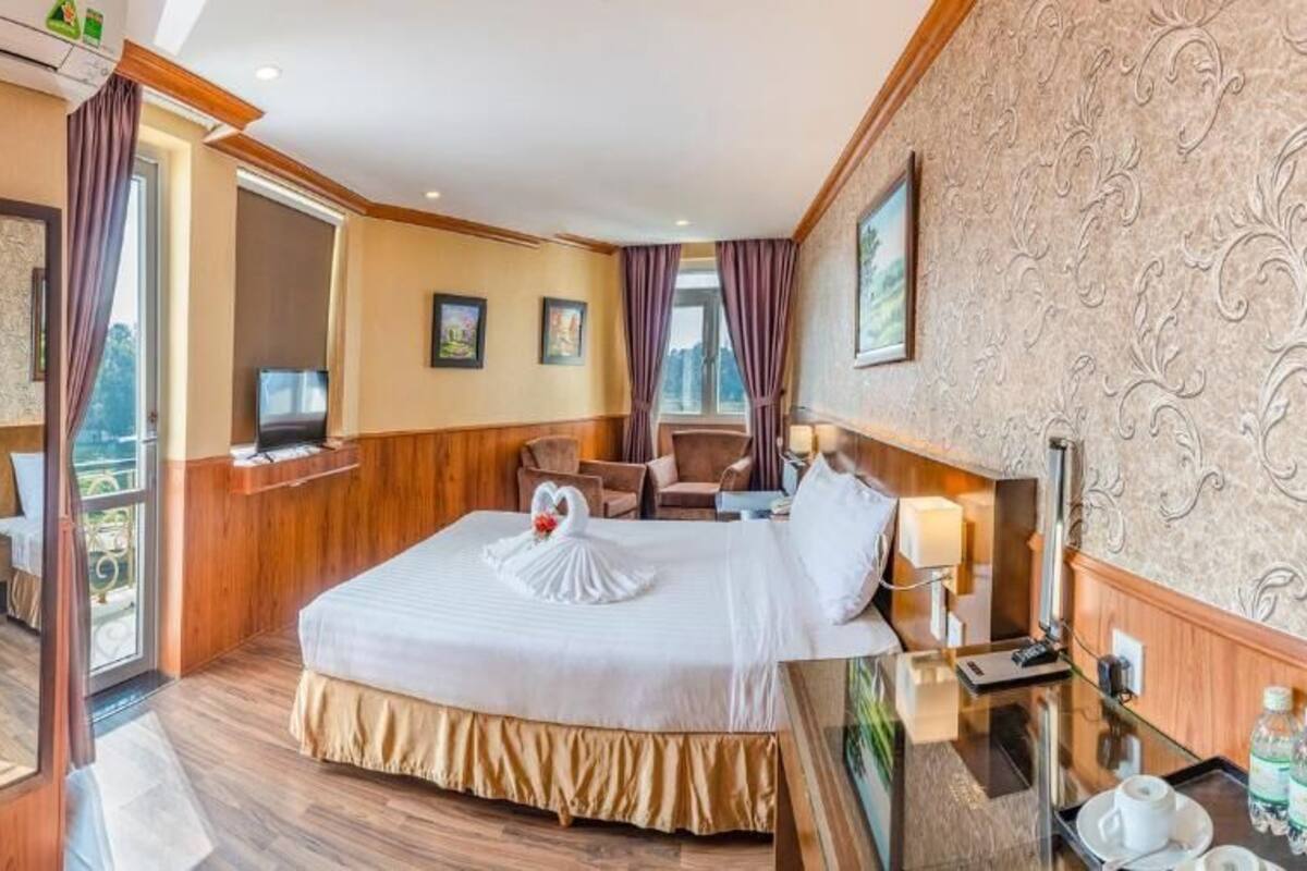 A hotel room with a large bed, a desk with a chair, a television, and a bathroom visible through an open door.