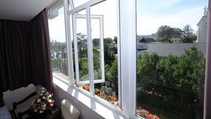 Et værelse med et stort vindue, en seng, en stol og et bord med blomster.