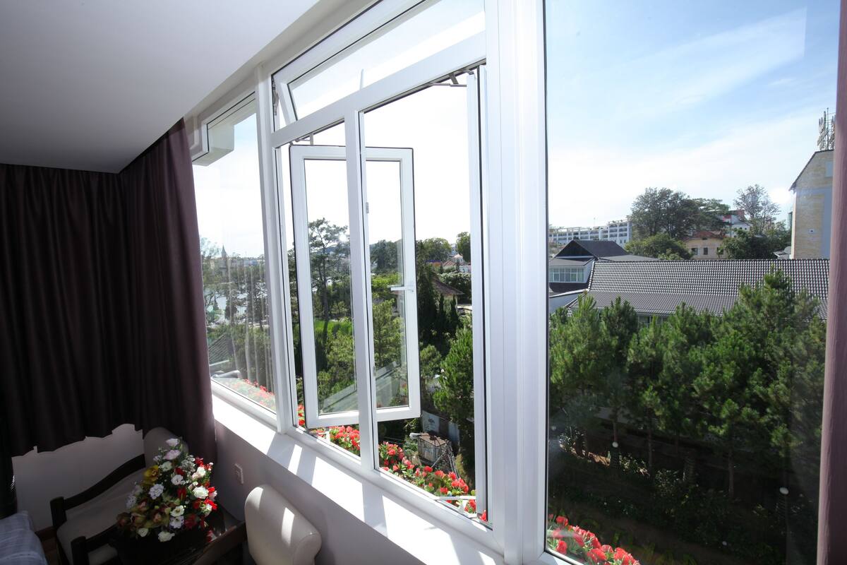 A room with a large window, a bed, a chair, and a table with flowers.