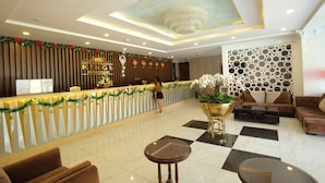 Een hotel receptie met een incheckbalie, een kroonluchter en een zithoek met banken en een salontafel.