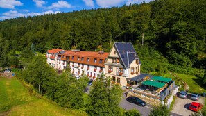 A large, multi-story hotel with a traditional European architectural style, surrounded by lush greenery and a forested hillside.