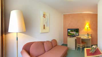 A cozy room with a sofa, a desk with a computer, a lamp, and a wall-mounted TV.