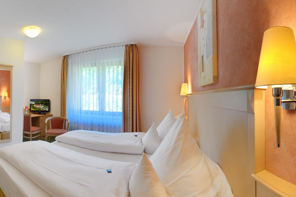 Une chambre d ’hôtel avec deux lits, un bureau, une chaise, une télévision et une salle de bain visible à travers une porte ouverte.