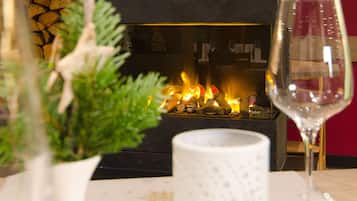 A fireplace with logs, a wine glass, and a white vase with greenery.