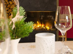 A fireplace with logs, a wine glass, and a white vase with greenery.