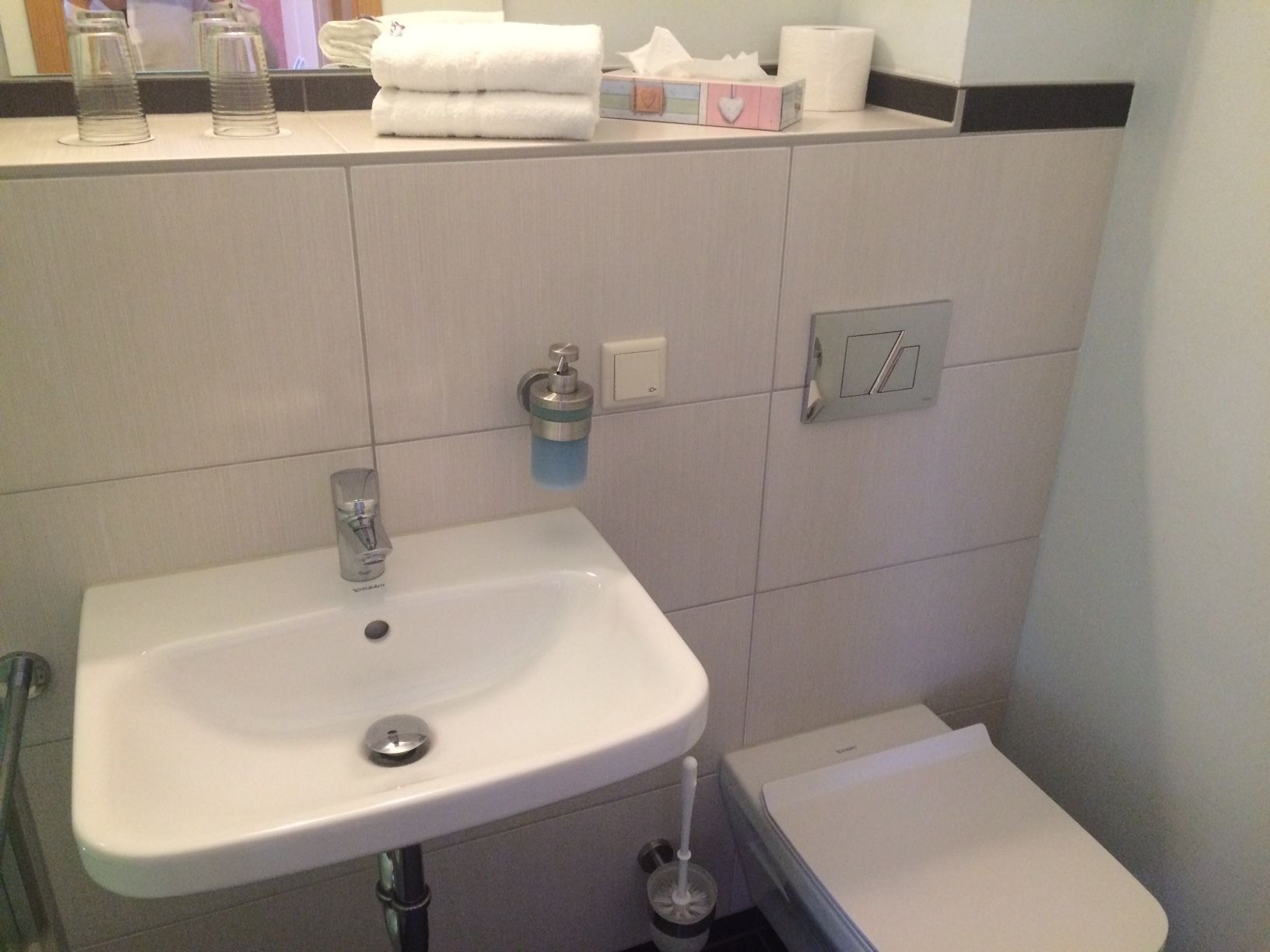 Un baño con un lavabo blanco, un inodoro y un estante con artículos de aseo.