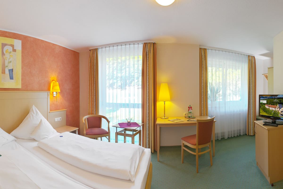 Une chambre d’hôtel comprenant un lit, un bureau, deux chaises, une télévision et une fenêtre avec des rideaux.