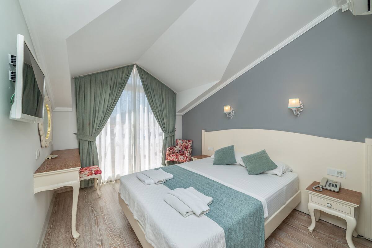 Ein Schlafzimmer mit Bett, Schreibtisch, Stuhl, Nachttisch mit Telefon und einer Wandleuchte.
