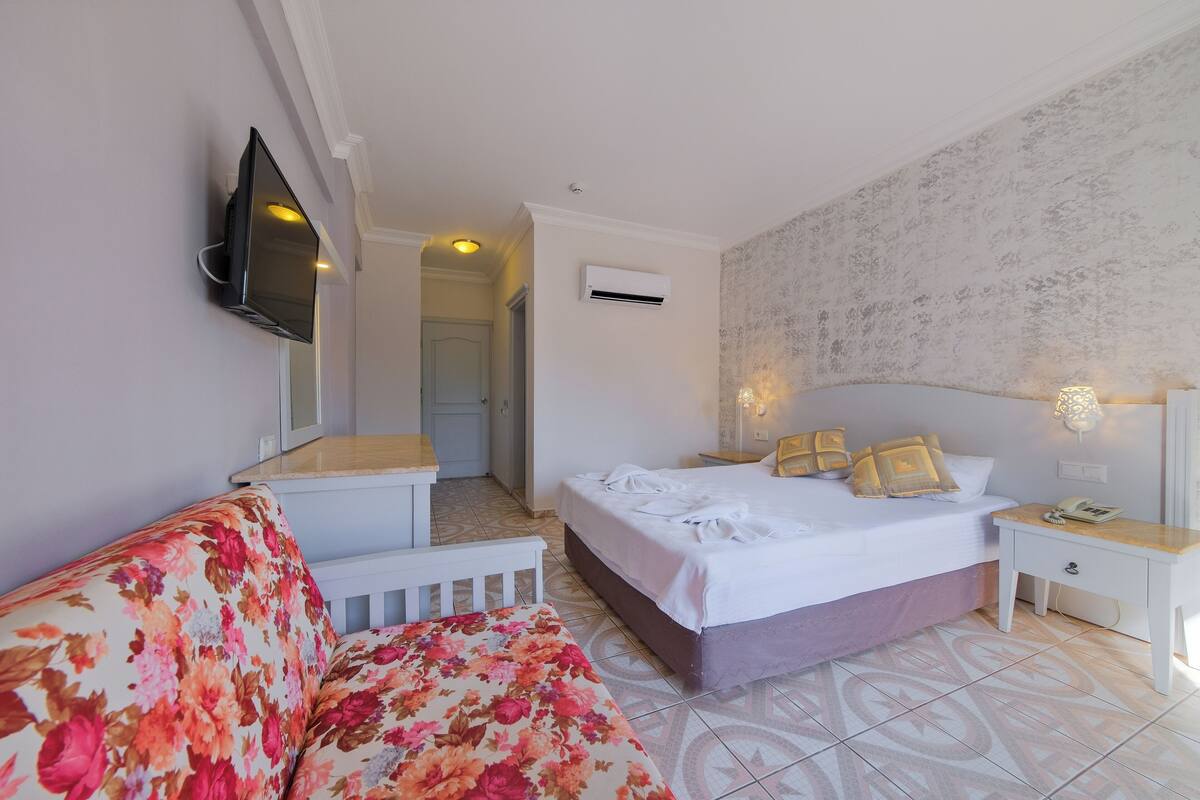 Ein Hotelzimmer mit einem Bett, einem Sofa, einem Fernseher, einem Nachttisch und einer Klimaanlage.