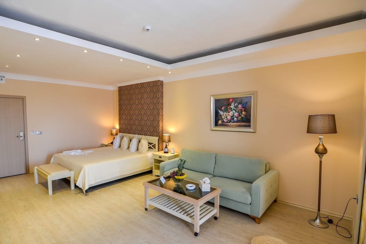 A hotel room with a bed, a sofa, a coffee table, a lamp, and a painting on the wall.