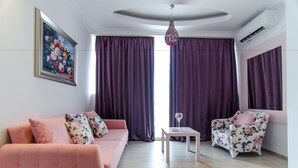 A modern living room with a pink sofa, a floral armchair, a small table, and purple curtains. - Phoenicia Luxury (Navodari)