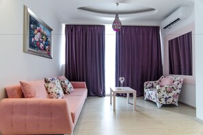 A modern living room with a pink sofa, a floral armchair, a small table, and purple curtains. - Phoenicia Luxury (Navodari)