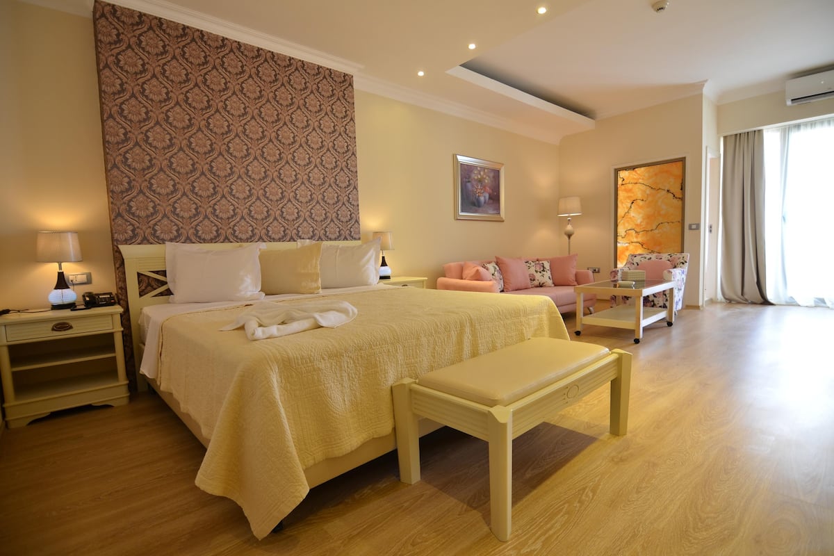 A hotel room with a large bed, a bench, a sofa, and a desk.