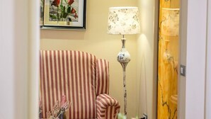 A striped sofa, a lamp, a framed picture of roses, and a mirror reflecting a door with a marble design. - Phoenicia Luxury (Navodari)