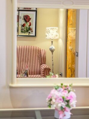 A striped sofa, a lamp, a framed picture of roses, and a mirror reflecting a door with a marble design. - Phoenicia Luxury (Navodari)