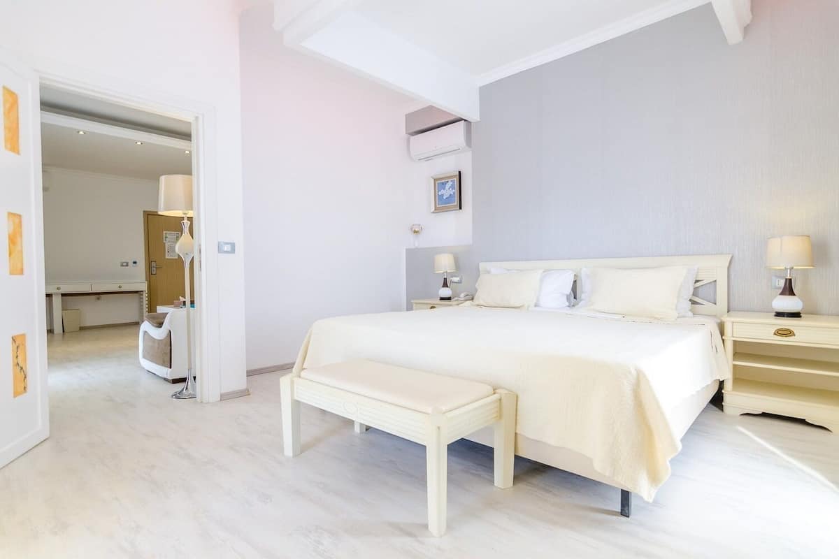 A modern bedroom with a large bed, bedside tables, a bench, and a desk.