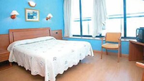 Quarto de hotel com cama, escrivaninha, cadeira e janela com cortinas.