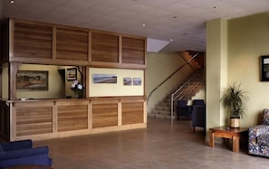 A reception area with a wooden reception desk, a staircase, and seating arrangements. - Soraya (Suances)