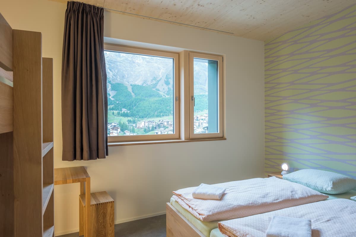 A bedroom with a bed, a window with curtains, a bedside table, and a patterned wall.