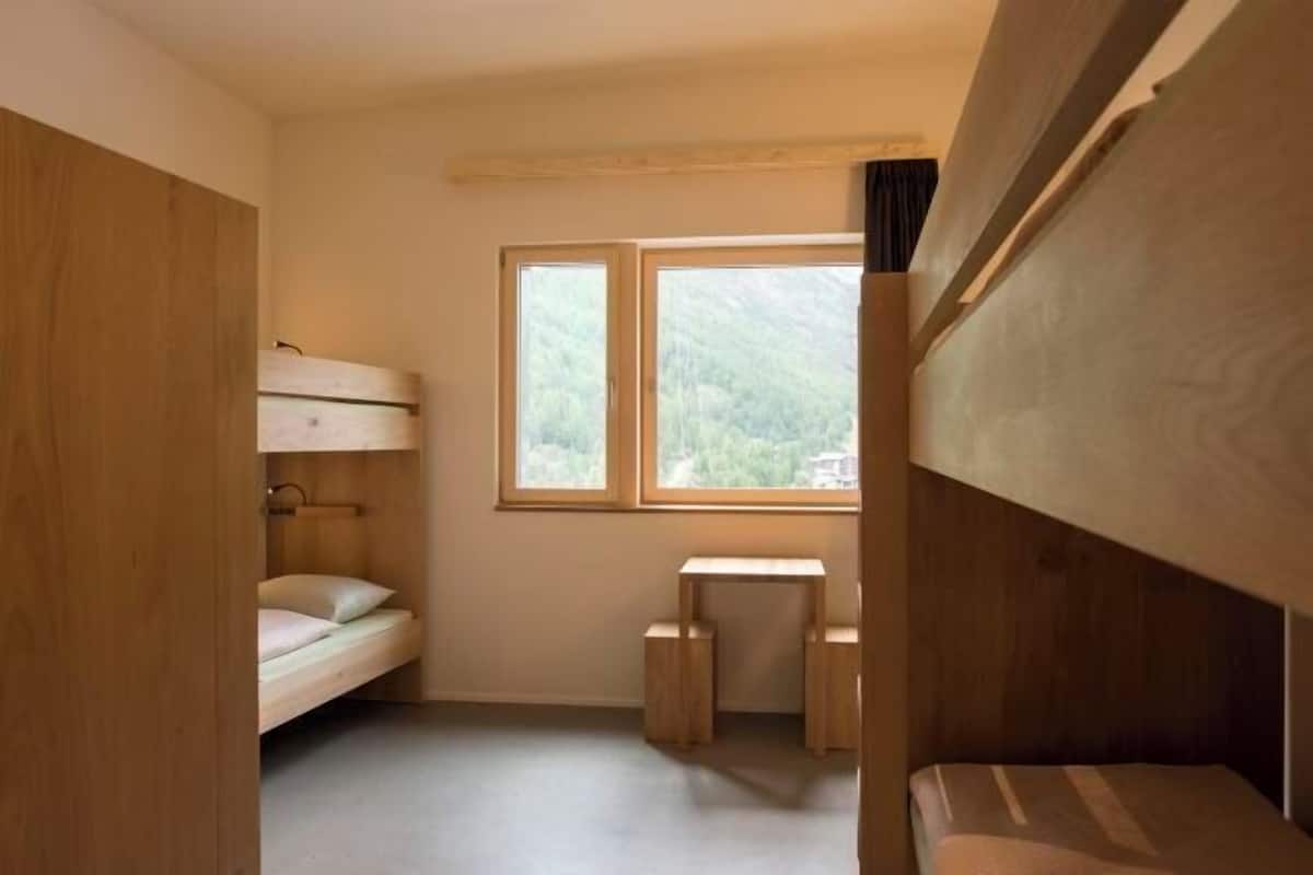 A compact room with bunk beds, a small table, and a window with a view of greenery.
