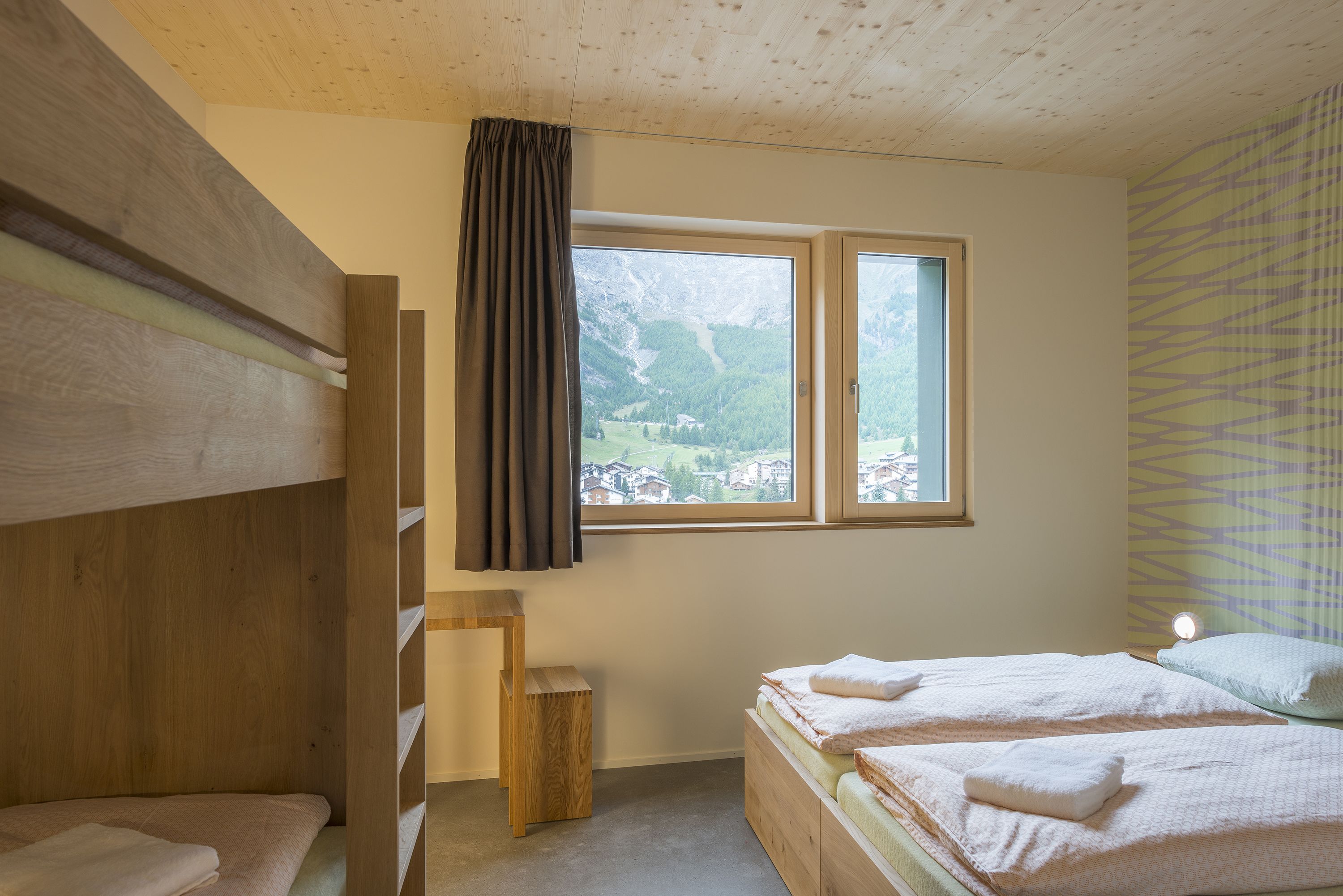 A bedroom with two beds, a wooden headboard, a window with a view of a mountain, and a patterned wall.