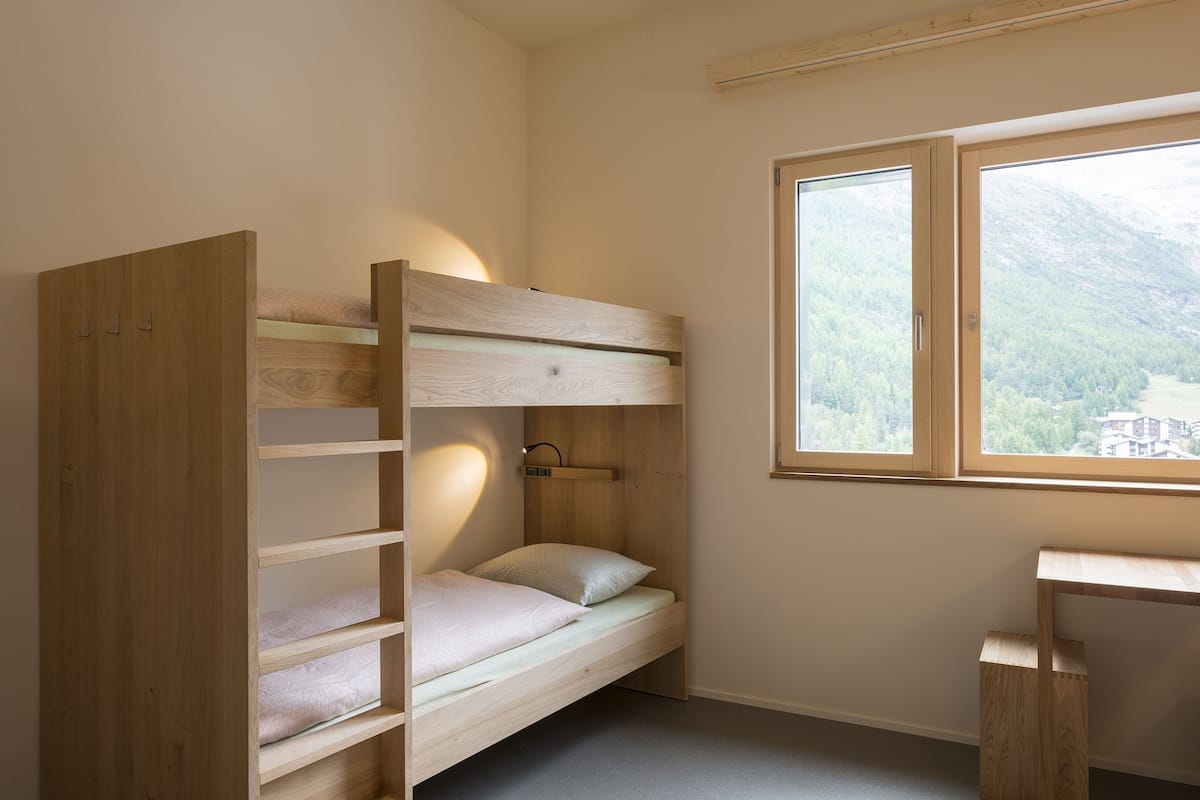 A bunk bed with a desk and a window with a mountain view.