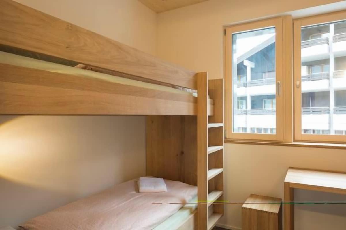 Dormitorio con literas, una ventana, un escritorio y un mueble pequeño.
