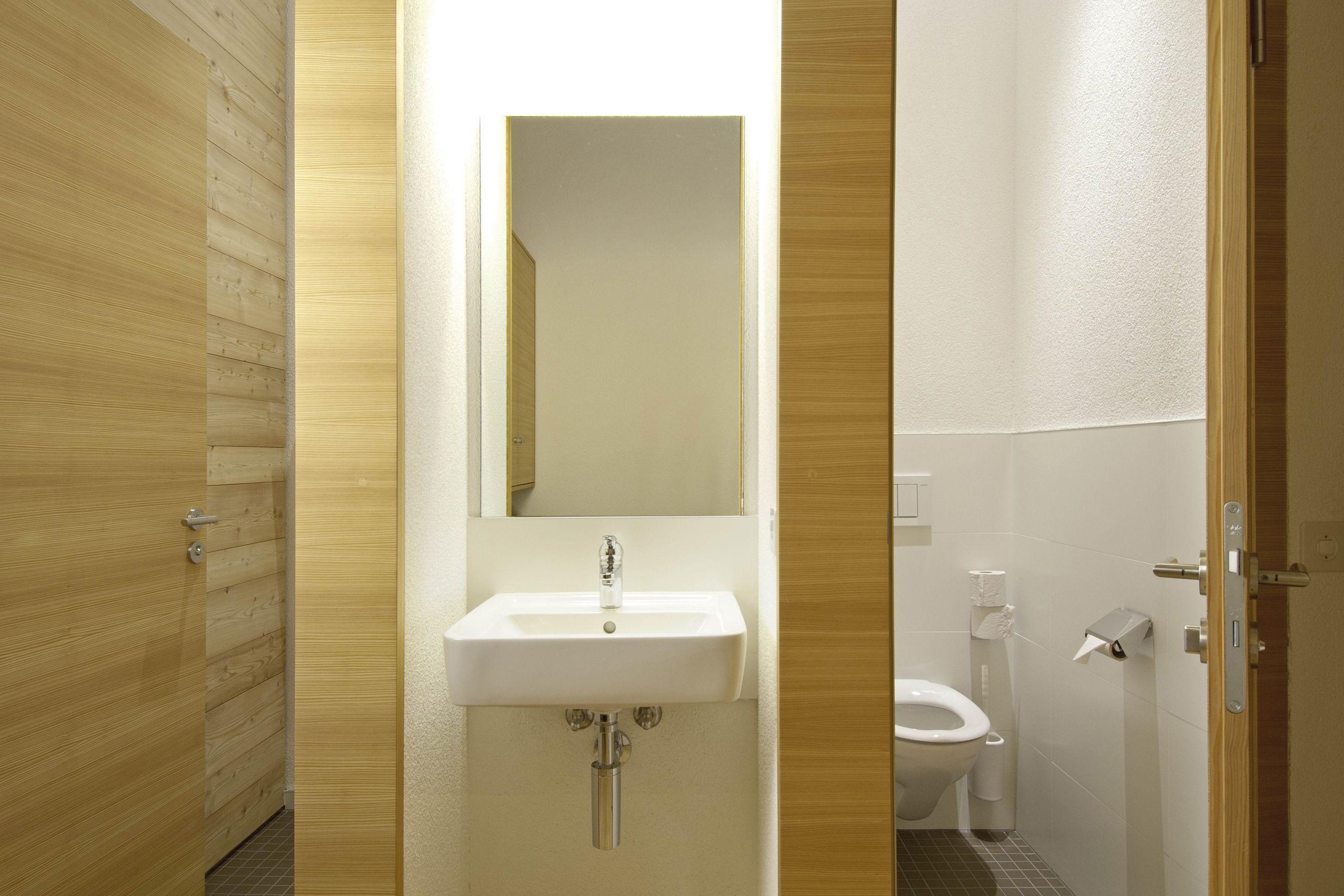 Un baño con tocador de madera, lavamanos, espejo y retrete.