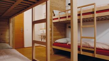 Une chambre avec deux lits superposés, un plancher en bois, une porte et une petite table de chevet avec une lampe.