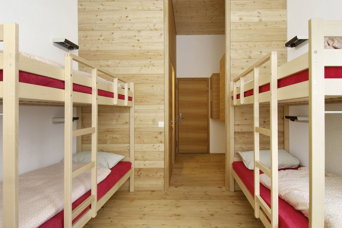 A room with two bunk beds, wooden walls, and a door leading to another room.