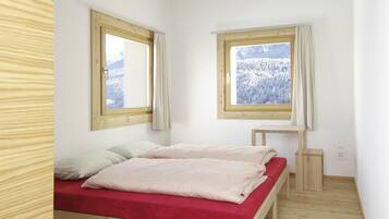 Un dormitori amb llit de fusta, dues finestres amb cortines i vista a un paisatge nevado.