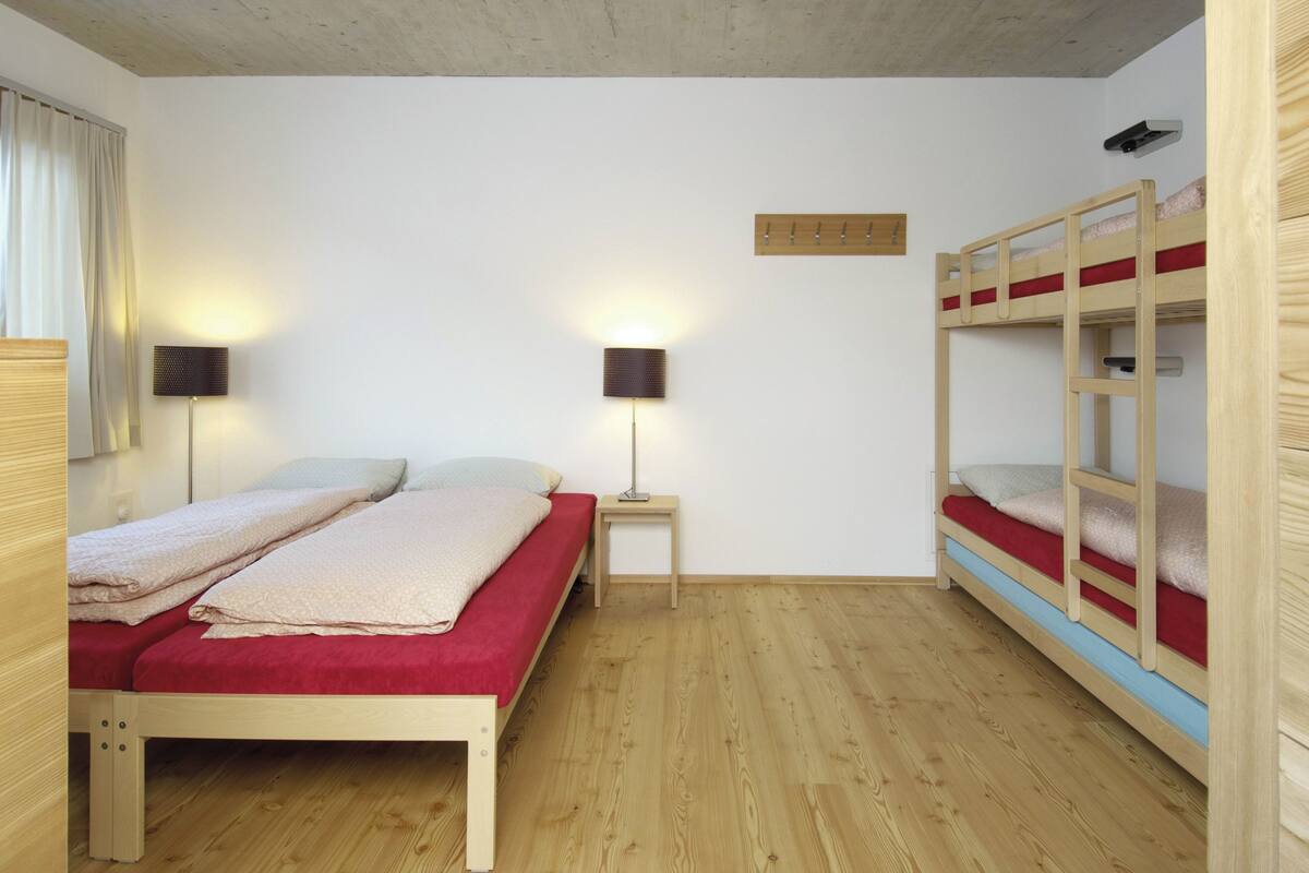 A room with two beds, a nightstand, a wall-mounted shelf, and a wooden ceiling.