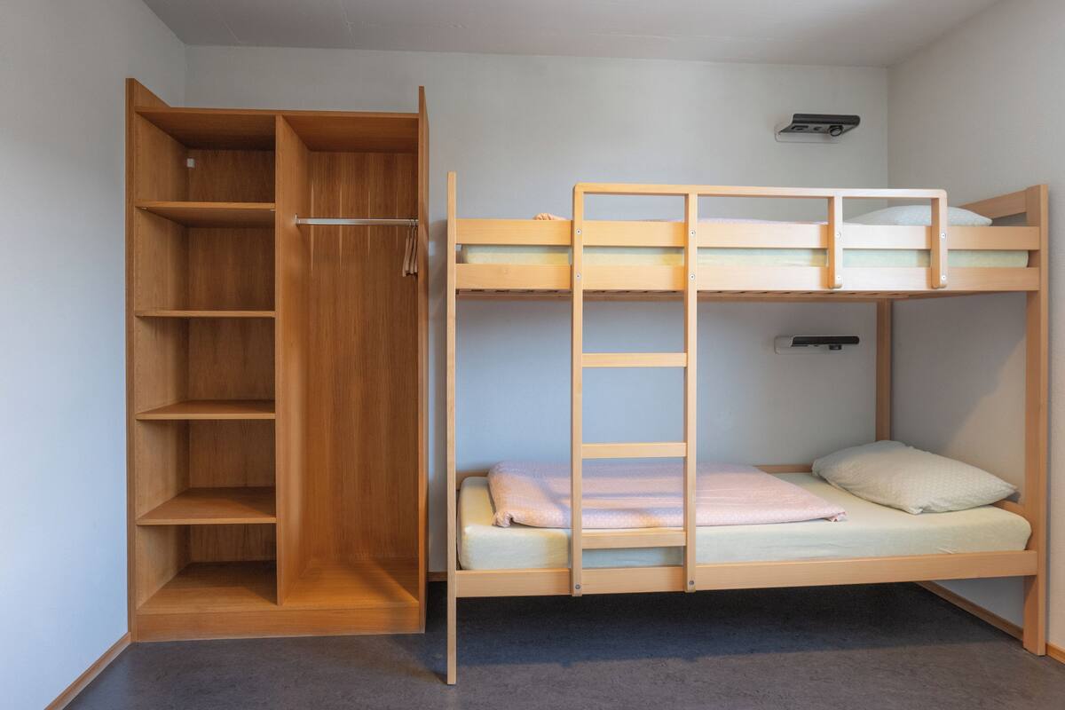 Una cama individual superpuesta con un armario de madera y estantes, una escalera y una pequeña unidad de almacenamiento.