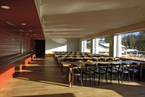 Un amplio comedor interior con varias mesas y sillas, ventanas grandes que dejan entrar luz natural, y vistas al exterior.